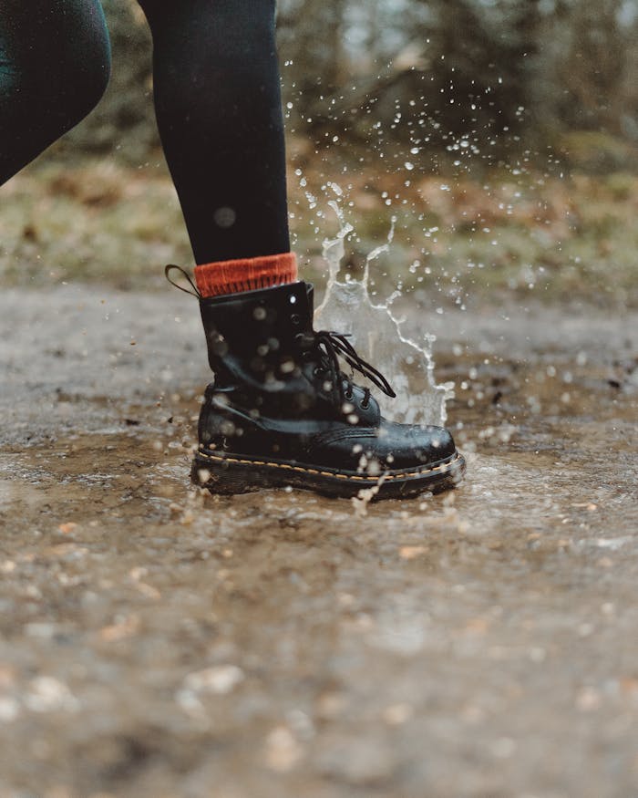 Close-up of waterproof boots splashing through a puddle on a rainy day outdoors.